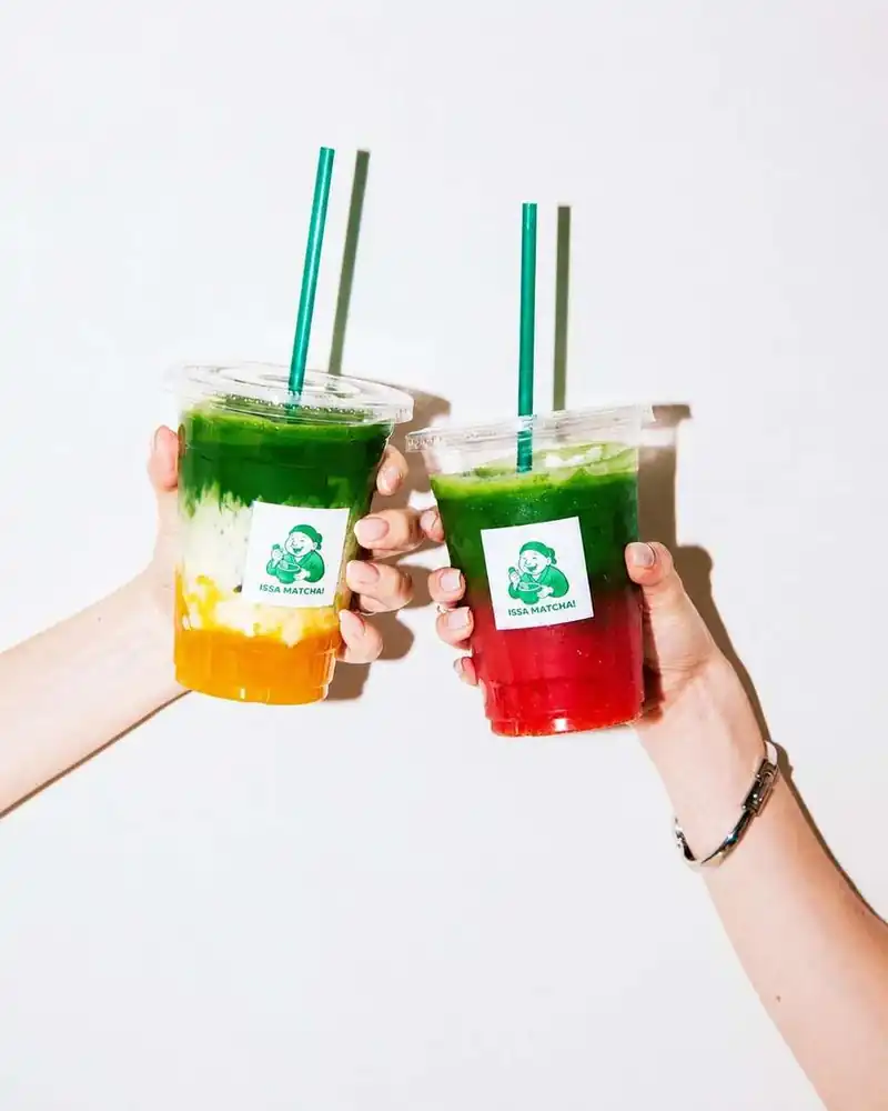 Two matcha drinks, mango and strawberry, raised in a toast